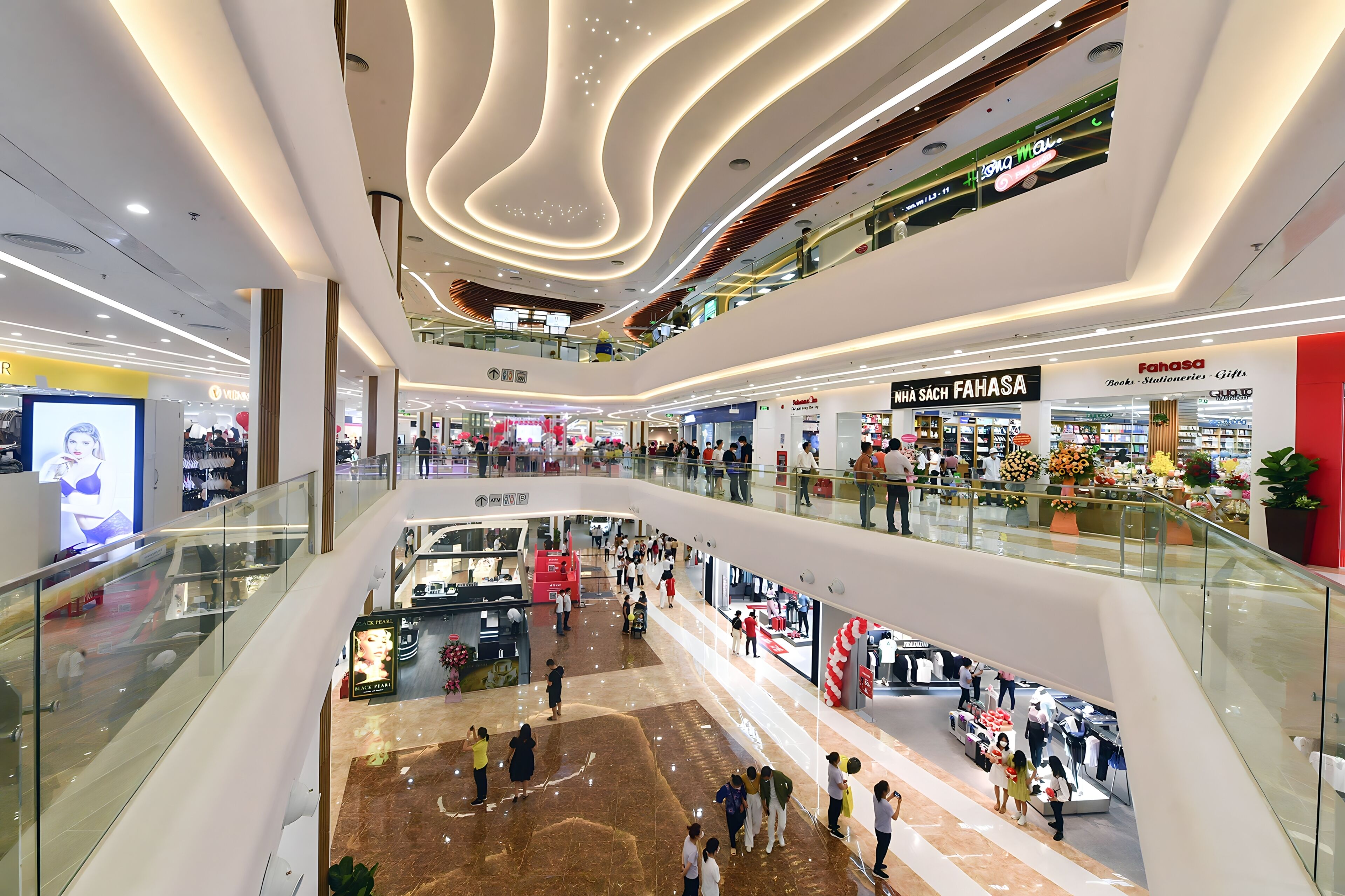 Un centro comercial de varios niveles con barandillas de vidrio, diversas tiendas y un espacio central abierto.