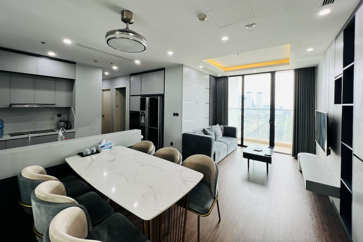 Una cocina moderna con encimera de mármol, comedor con mesa y sillas, un sofá y un amplio ventanal con vistas a la ciudad.