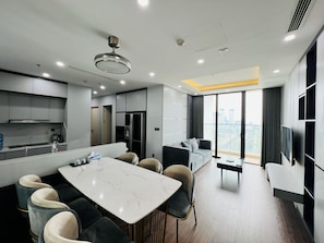 Una cocina moderna con encimera de mármol, comedor con mesa y sillas, un sofá y un amplio ventanal con vistas a la ciudad.