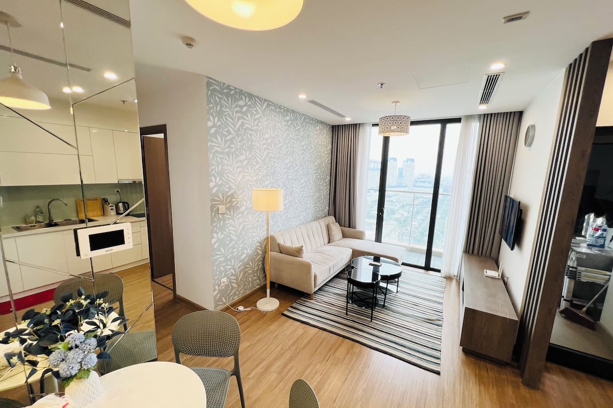 Una habitación de hotel moderna con cocina, sala de estar con sofá y mesa de centro, y un ventanal con vista a la ciudad.