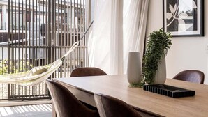 A dining area with a wooden table, chairs, a hanging hammock, a potted plant, and a framed artwork. - Aurelia Byron- Jonson Lane (Byron Bay)