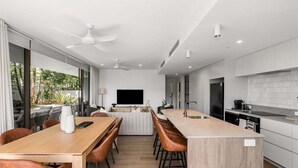 A modern kitchen with a central island, a dining area with chairs, and a TV mounted on the wall. - Aurelia Byron- Jonson Lane (Byron Bay)