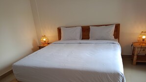 Un lit bien fait, avec du linge de lit blanc, une tête de lit en bois et deux lampes de chevet posées sur des tables de chevet en bois.