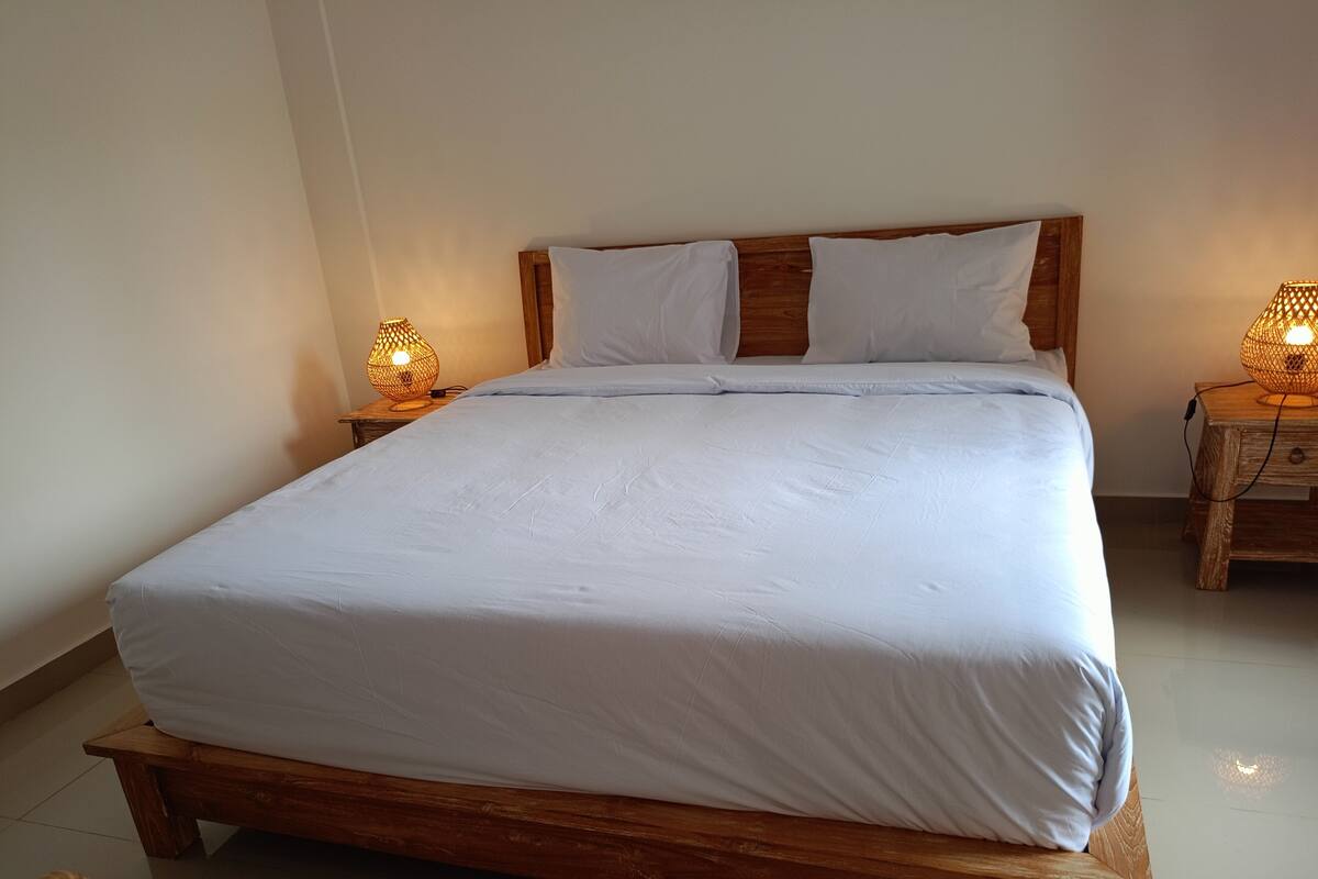 A neatly made bed with white linens, wooden headboard, and two bedside lamps on wooden nightstands.