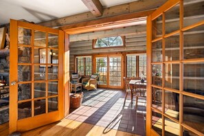 A log cabin interior with a stone fireplace, a dining area with a table and chairs, and large windows allowing natural light. - Waterfront Log Home Near Sister Bay- Game Room, Kayaks & Sunrises (Sister Bay)