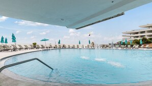 Una amplia piscina al aire libre con numerosas tumbonas y sombrillas, rodeada por un edificio bajo un cielo despejado.