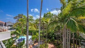 Un complexe hôtelier doté d’une piscine, de palmiers et surplombant un ciel bleu azur.