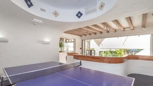 Une table de ping-pong dans une pièce dotée d’un plafond voûté, de poutres en bois et offrant une vue sur la verdure à l’extérieur.