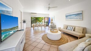 Un vaste espace de vie comprenant un téléviseur à écran plat, un canapé, une table basse ronde et un coin repas avec une table et des chaises.