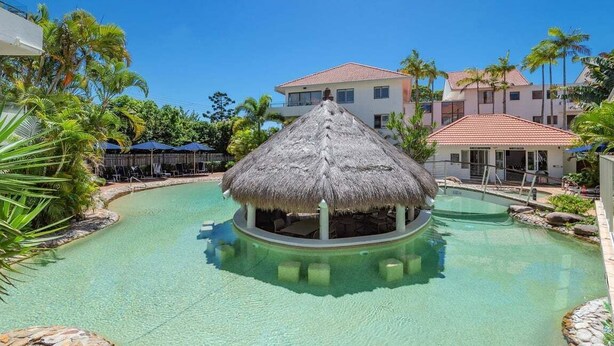 Un complexe hôtelier doté d’une piscine centrale, d’une structure à toit de chaume et d’une végétation tropicale.