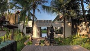 Eingang eines tropischen Resorts mit Holzterrasse, Palmen und einem Wasserspiel.