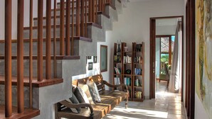 Eine Treppe mit hölzernen Geländern, ein Bücherregal voller Bücher und ein Blick ins Freie durch eine Tür.