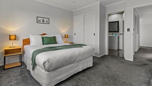 A hotel room with a large bed, two bedside tables with lamps, a wardrobe, and a bathroom visible through an open door. - Modern Townhouse with Parking nr Airport & Manukau (Auckland South)