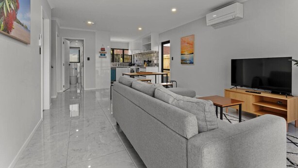 A modern living room with a grey sectional sofa, a wooden TV stand, and a flat-screen TV. - Modern Townhouse with Parking nr Airport & Manukau (Auckland South)