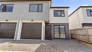 A two-story residential building with a garage, a front door, and a wooden fence. - Modern Townhouse with Parking nr Airport & Manukau (Auckland South)