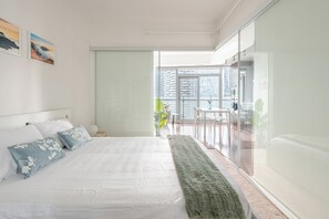 A modern bedroom with a large bed, a green throw blanket, and a view of a balcony with outdoor furniture. - Modern 1BR | WFH Desk+Monitor | FastWiFi | Kitchen (Toronto)