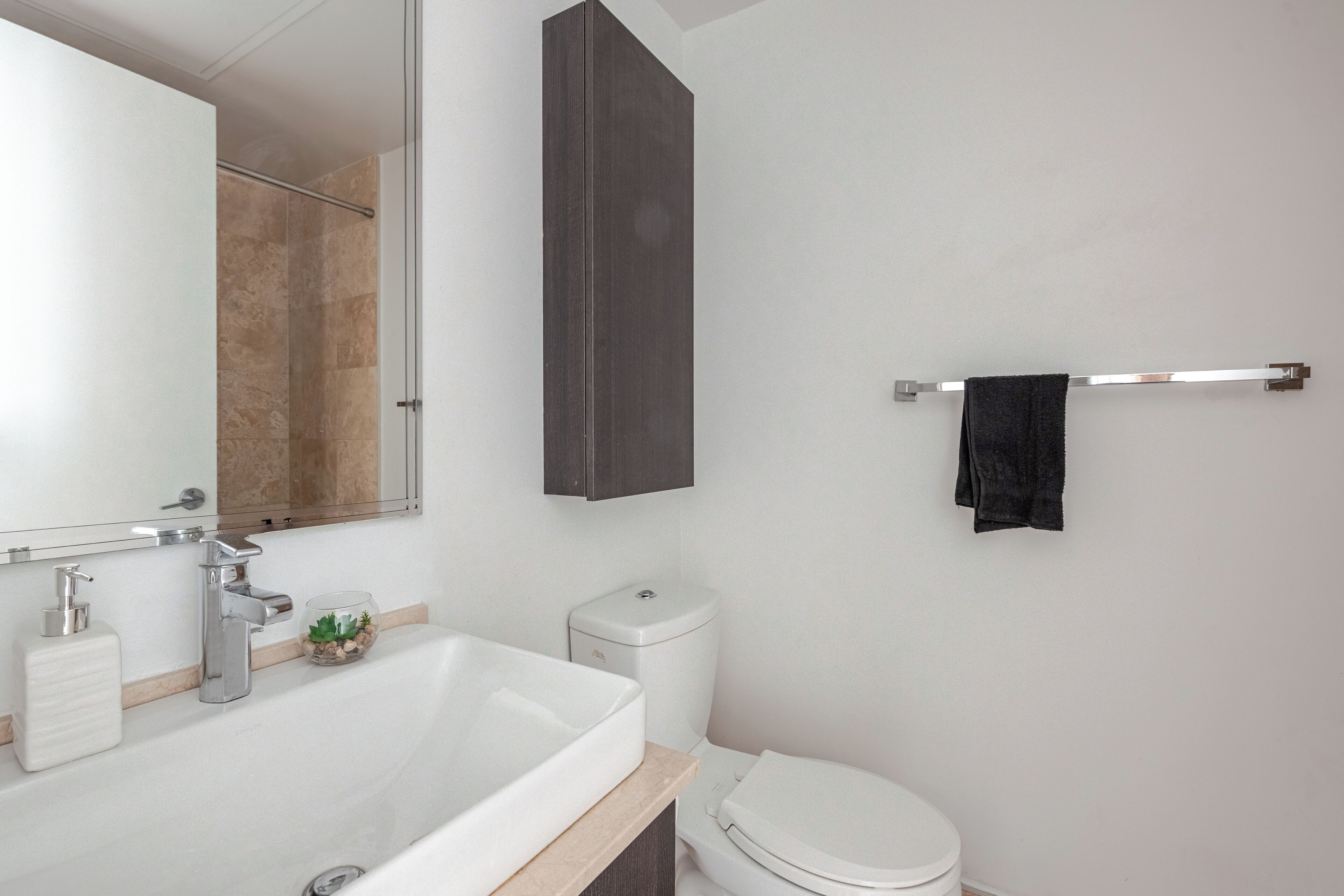 Une salle de bain moderne avec un lavabo blanc, un miroir, un meuble sombre, des toilettes et un porte-serviettes.