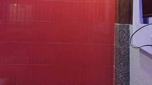 Une pièce aux murs recouverts de carreaux rouges, avec un panneau de bois et un mur blanc percé d’une fenêtre.