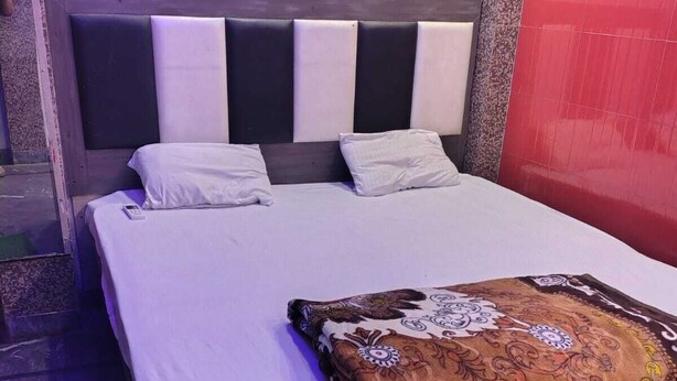 Un lit avec une couverture à motifs, une tête de lit composée de panneaux clairs et foncés alternés, et un mur d’accent rouge.