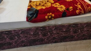 Un lit avec une tête de lit blanche et deux oreillers, un plaid à motifs floraux rouges et une table de chevet en marbre foncé.