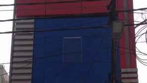 Un immeuble à plusieurs étages, doté d’une façade bleue et rouge, avec une grande fenêtre circulaire à l’étage supérieur et une entrée de garage au niveau du rez-de-chaussée.