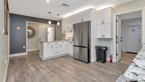 Una cocina moderna con armarios blancos, un refrigerador de acero inoxidable y piso de madera.