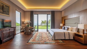 Una habitación de hotel moderna con una cama grande, una zona de comedor con mesa y sillas, un televisor y vistas al océano.