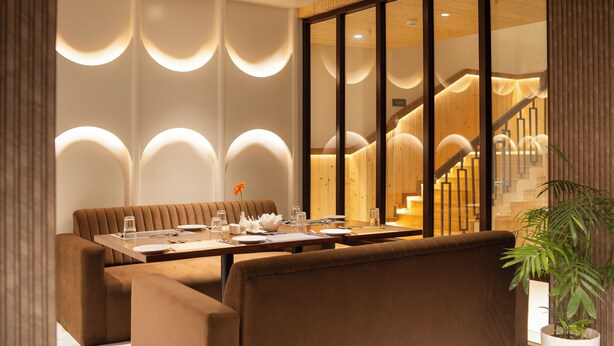 Un comedor con una mesa larga, asientos acolchados y una escalera al fondo.