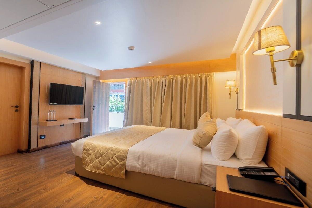 A hotel room with a bed, bedside table, TV, and a view of the outdoors.