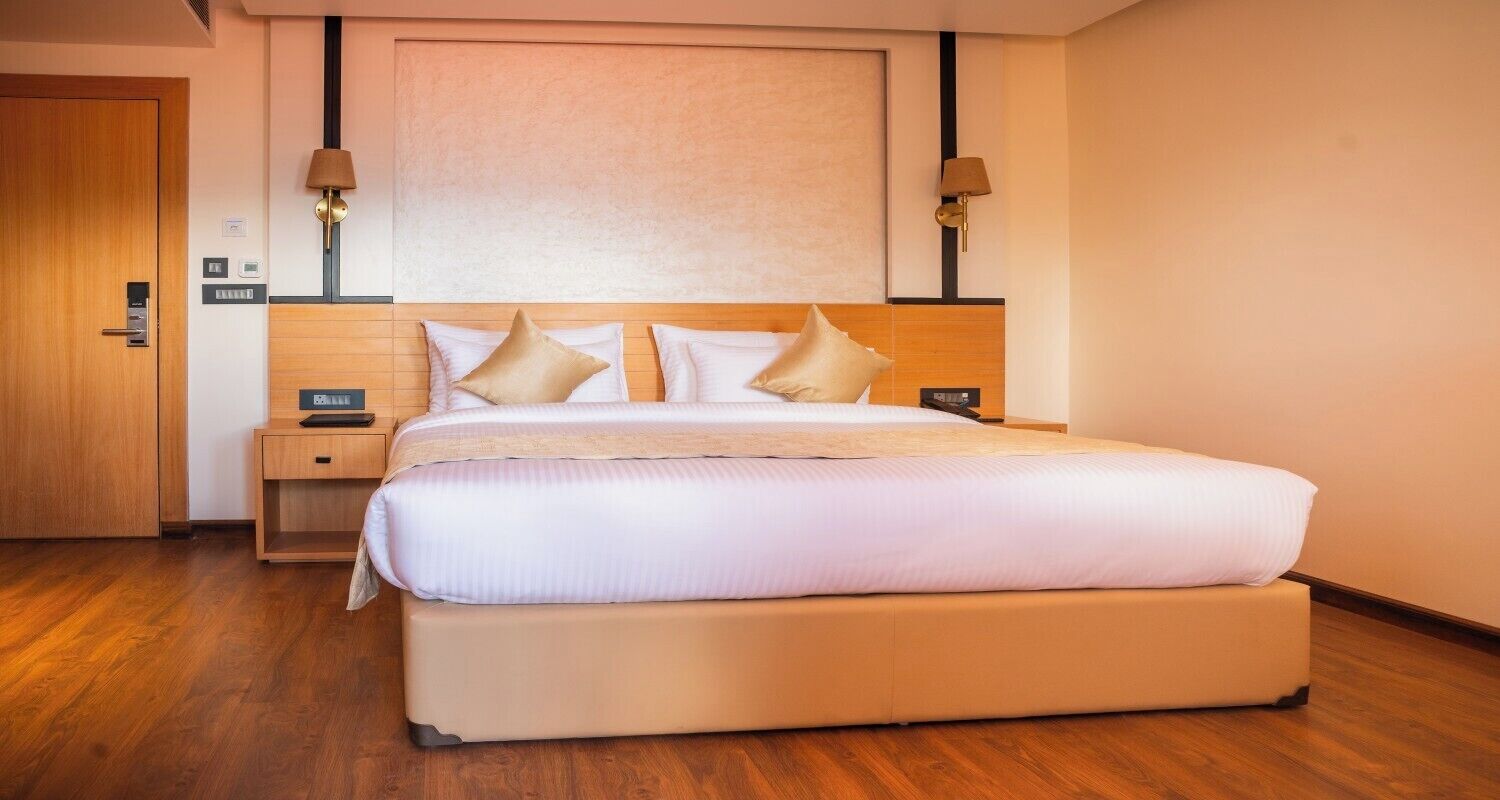 A hotel room with a large bed, wooden headboard, two bedside tables, and two wall-mounted lamps.