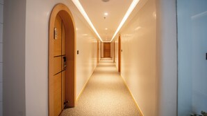 Un pasillo largo y estrecho con puertas de madera a la izquierda y una pared blanca a la derecha.