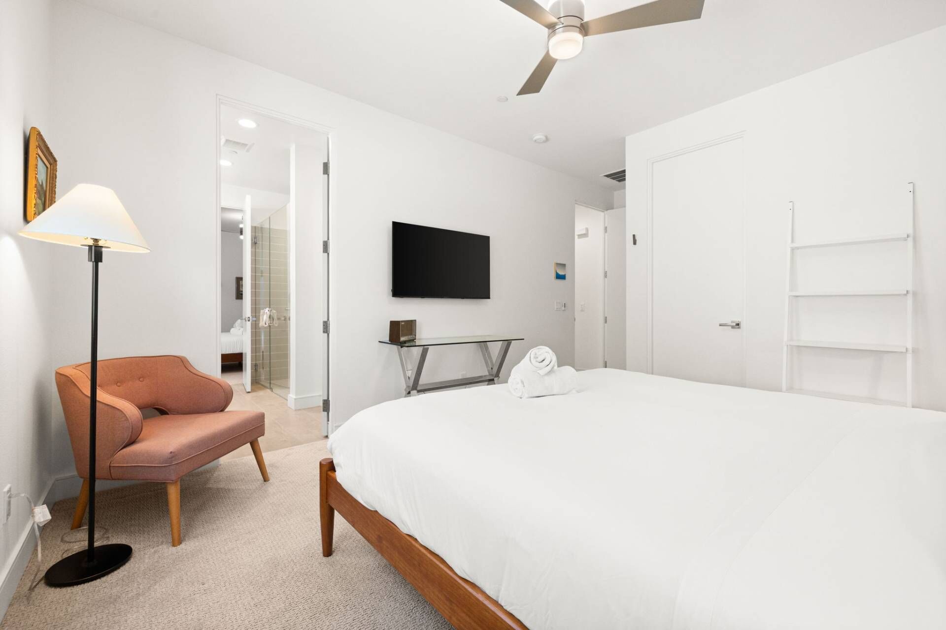 Ein modernes Hotelzimmer mit einem großen Bett, einem flachbildfernseher an der Wand, einer Stehlampe, einem Sessel und einem begehbaren Kleiderschrank.