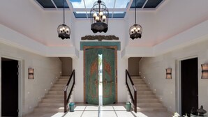 Eine imposante Treppe mit einer großen, verzierten Tür am oberen Ende, die zu einem hellen, gut beleuchteten Innenraum mit Oberlicht und dekorativen Leuchten führt.