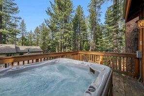 Un jacuzzi en una terraza de madera con vista a altos pinos.
