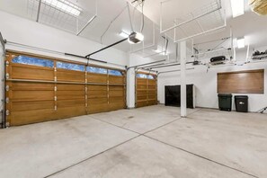 Un garaje espacioso con grandes puertas de madera, piso de concreto y techo alto con vigas y luminarias a la vista.