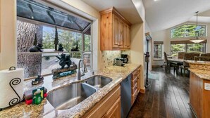 A kitchen with granite countertops, wooden cabinets, a large window, and a dining area with a view. - Tahoe Trailside Lodge: Hot Tub, AC, Walk-to-Trail (South Lake Tahoe)