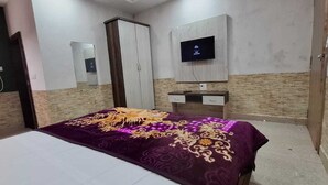 Um quarto com cama, guarda-roupa, televisão na parede e uma pequena escrivaninha com gavetas.