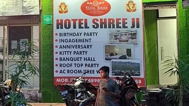 Um edifício com a placa do Hotel Shreeji, oferecendo comodidades como salão de festas e quartos com ar condicionado.