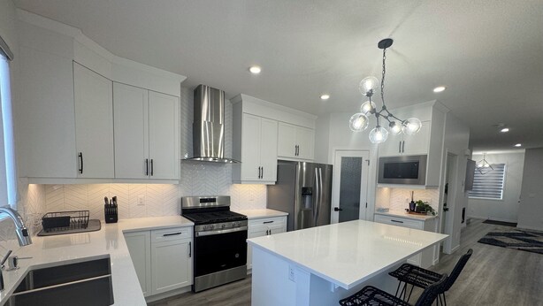 A modern kitchen with white cabinetry, stainless steel appliances, and a central island with bar stools. - Family-Friendly Calgary Retreat | Gateway to Banff (Calgary)