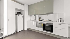 Een moderne keuken met witte kasten, een magnetron, een koelkast, een vaatwasser, een oven en een koffiezetapparaat.
