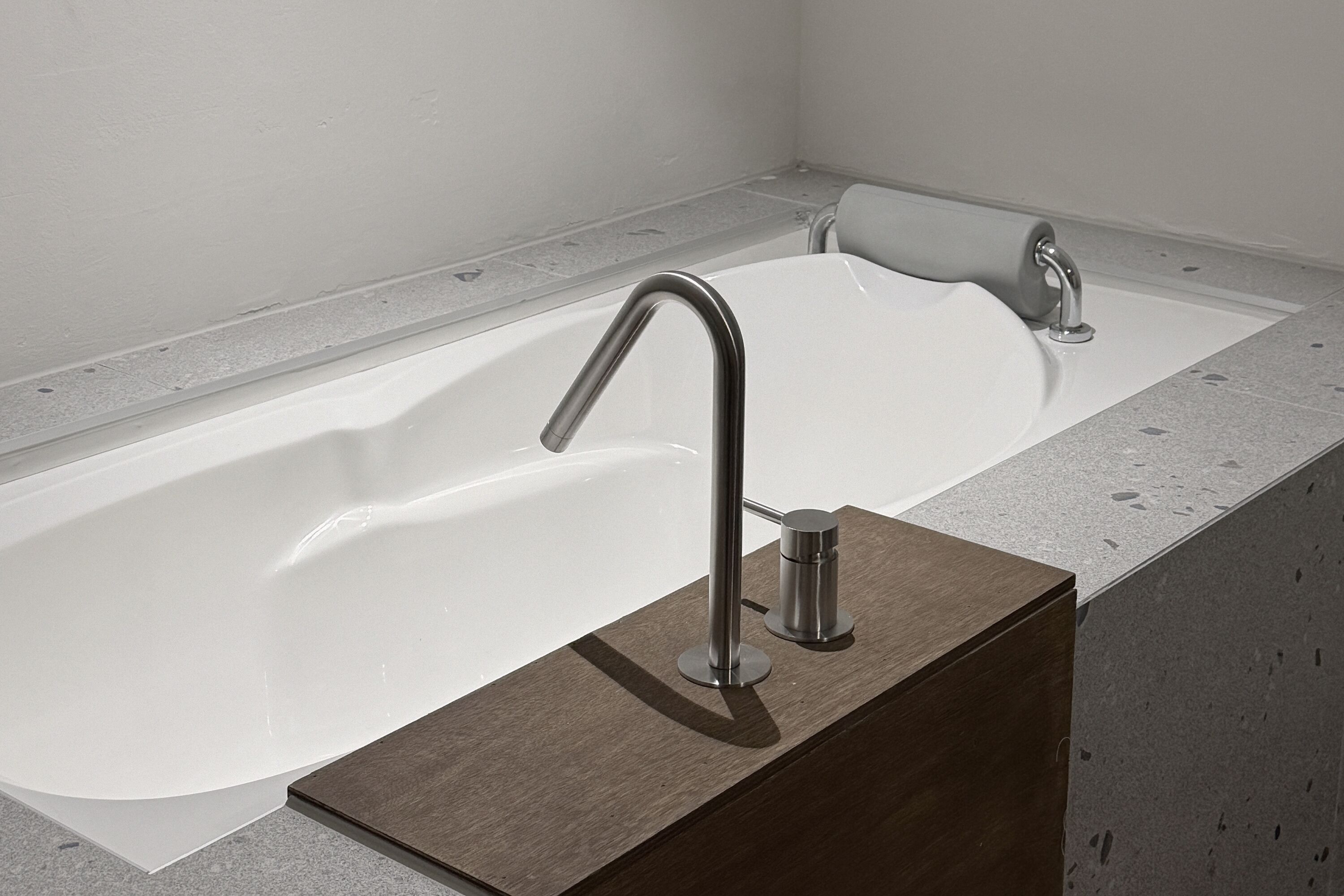 A modern bathroom with a large white bathtub, a wooden vanity, and a sleek faucet.