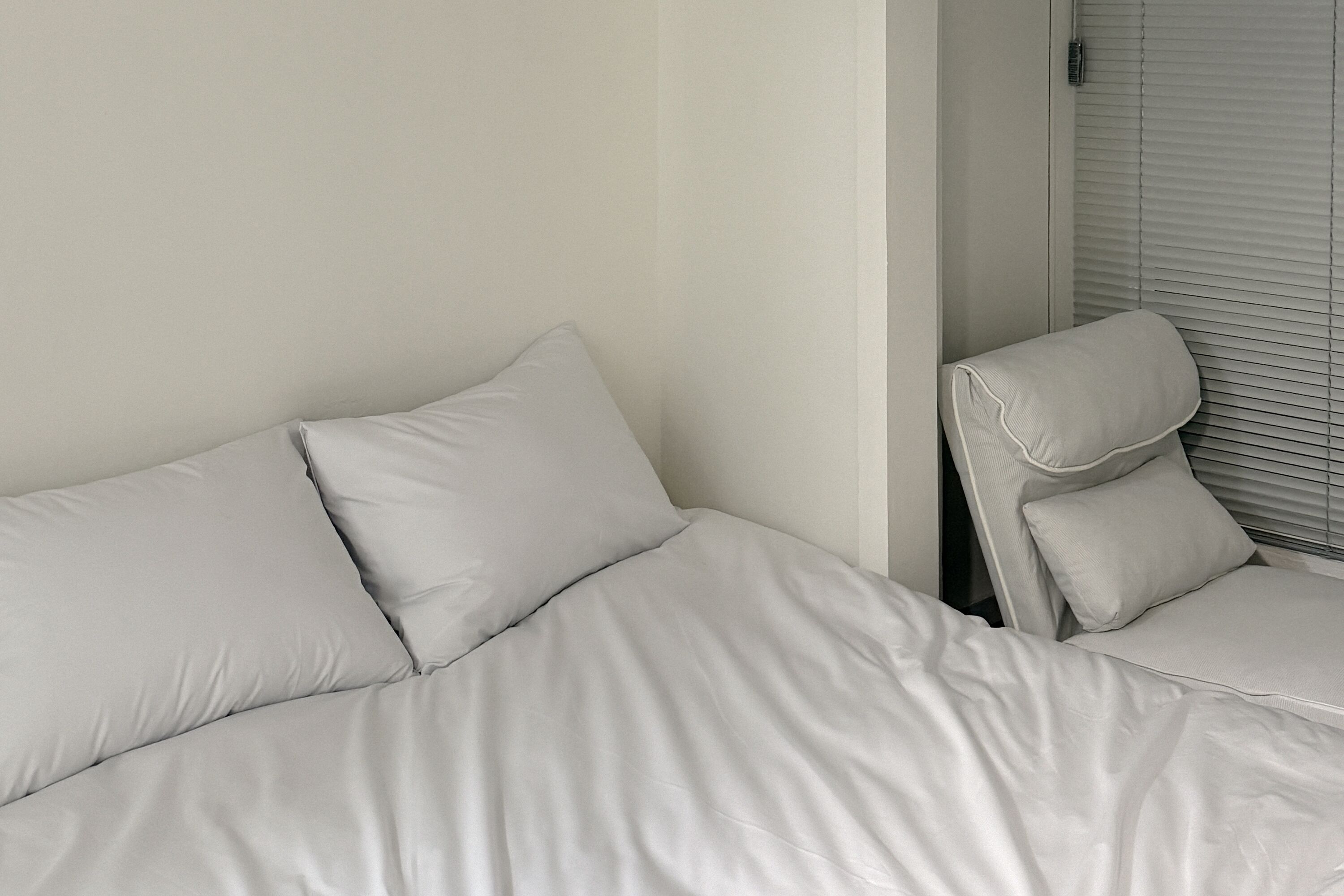 Una cama con ropa de cama blanca y una silla con cojín.