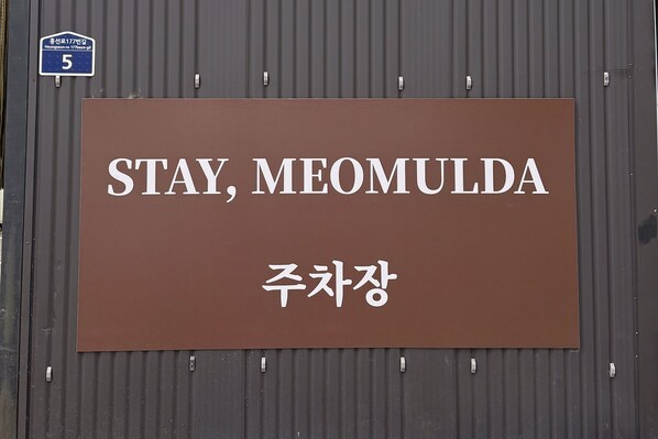 Un letrero con el texto 'STAY, MEOMULDA' y '주차장', que indica un área de estacionamiento.