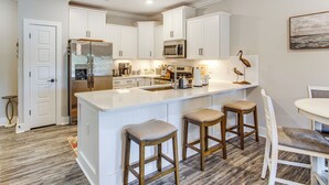 A modern kitchen with white cabinetry, a stainless steel refrigerator, a built-in oven, and a large island with bar stools. - Family Getaway in Calabash w/ Pool; 9 Mi to Beach (Calabash)