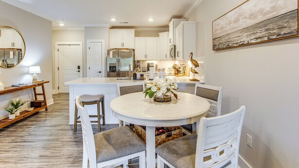 A modern kitchen with white cabinets, a central island, and a dining area with white chairs and a table. - Family Getaway in Calabash w/ Pool; 9 Mi to Beach (Calabash)