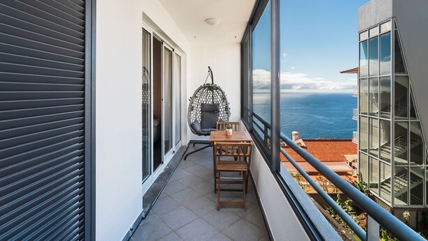 A balcony with a view of the sea, a hanging chair, and a table with chairs. - GuestReady - Charming Apartment with Ocean Views (Caniço)