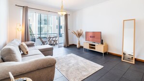 A modern living room with a sofa, TV, and a large mirror. - GuestReady - Charming Apartment with Ocean Views (Caniço)