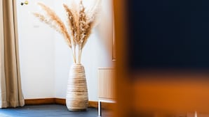 A room with a tall vase of pampas grass, a wooden cabinet, and a door with a brass handle. - GuestReady - Charming Apartment with Ocean Views (Caniço)