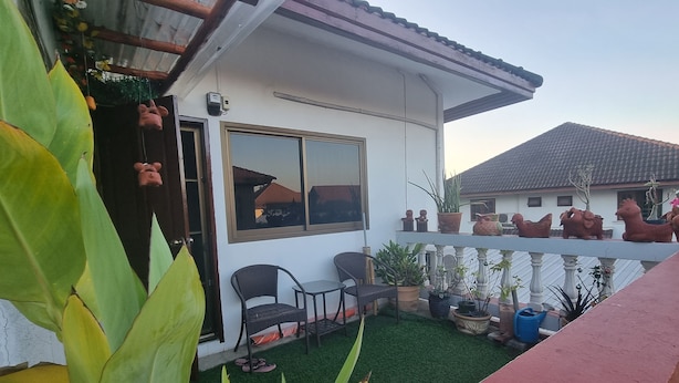 Een huis met een witte gevel, een balkon met potplanten, een klein terras met stoelen en een raam dat de omgeving weerspiegelt.