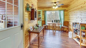 Ein Holzblockhaus-Interieur mit einem Esstisch, Stühlen, einem Bücherregal und einem Fenster mit Vorhängen.